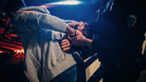 Male Policeman Forcing a Compliant Civilian on the Hood of Police Car. Officer Violently Pushing Man Against the Car and Handcuffing Him. Shocking Case of Police Brutality. Close up on Hands